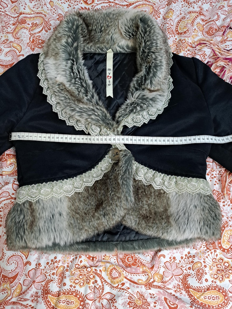 K&ouml;nnte beinhalten: Schwarze Bolerojacke mit Kunstfellbesatz und Spitzenkragen. Die Jacke hat einen Knopfverschluss und ein Etikett mit dem Text "my♡se". Die Jacke ist ca. 71 cm lang.