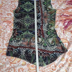 May include: A sleeveless top featuring a repeating butterfly wing pattern in shades of green, black, and brown, with a light purple trim at the neckline. A white measuring tape is placed vertically over the center, showing a length of 75 centimeters.
