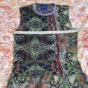 May include: A sleeveless top featuring a vibrant butterfly wing print in shades of green, brown, and black. A white measuring tape is placed across the chest, showing a width of approximately 41 centimeters. The garment has a round neckline with a light purple trim and a Kenzo Jeans label at the collar.
