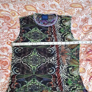 May include: A sleeveless Kenzo Jeans top featuring a vibrant, symmetrical butterfly wing print in shades of green, black, and brown. A white measuring tape across the chest indicates a width of approximately 16 inches. The neckline has a purple trim.