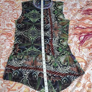 May include: A sleeveless top featuring a vibrant, symmetrical butterfly wing pattern in shades of green, brown, and black. A white measuring tape is placed vertically over the center, showing a length of approximately 30 inches from neck to hem.