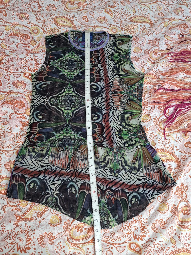 May include: A sleeveless top featuring a vibrant, symmetrical butterfly wing pattern in shades of green, brown, and black. A white measuring tape is placed vertically over the center, showing a length of approximately 30 inches from neck to hem.