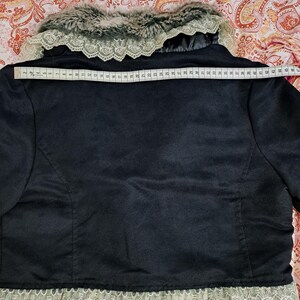 K&ouml;nnte beinhalten: Schwarze Jacke mit Kunstfellkragen und -besatz. Die Jacke hat eine Spitzendetail am unteren Rand. Die Breite der Jacke betr&auml;gt ca. 114 cm am R&uuml;cken.