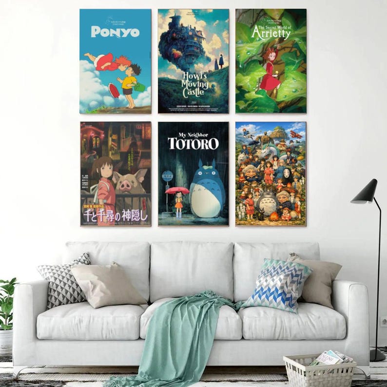 May include: Six framed movie posters featuring animated films, including "Ponyo," "Howl's Moving Castle," and "My Neighbor Totoro." The posters are displayed on a white wall above a white sofa with decorative pillows and a green throw blanket.