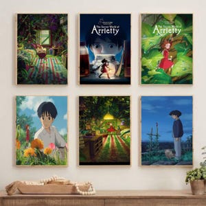 May include: Six framed art prints featuring scenes from "The Secret World of Arrietty" anime film. The prints showcase colorful illustrations of characters and environments, with vibrant greens, reds, and blues. The artwork is displayed on a wooden surface.