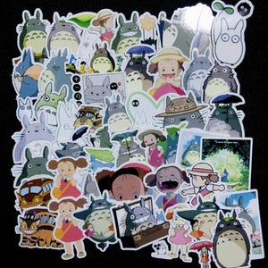 Pu&ograve; includere: Una collezione di adesivi colorati con personaggi e scene del film d'animazione "Il mio vicino Totoro". Gli adesivi raffigurano vari personaggi di Totoro, ragazze e altri elementi del film, con sfondo nero.