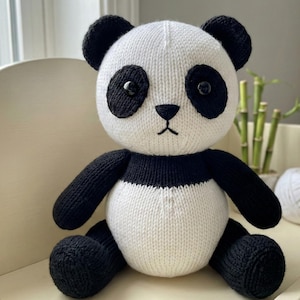 May include: A knitted panda bear toy with a white body and black features, including ears, eyes, arms, and legs. The panda has a black nose and a stitched mouth. The toy is sitting on a white surface.