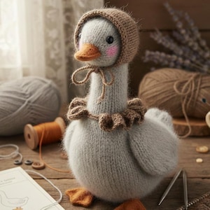 May include: A handmade knitted goose doll, wearing a brown bonnet and ruffled collar. The goose has an orange beak and feet, with pink cheeks. The scene includes yarn, sewing notions, and a book, suggesting a craft or nursery theme.