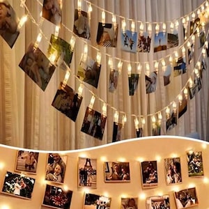 May include: A string of warm white LED lights with small clear clips holding various photographs. The lights are strung across a beige curtain. The photographs are of different sizes and feature people and scenes.