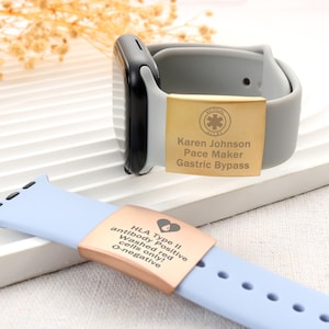 Puede incluir: Un reloj inteligente con una correa gris y una etiqueta de alerta médica dorada. La etiqueta está grabada con el nombre "Karen Johnson" e información médica. También se muestra una correa de reloj azul claro con una etiqueta de alerta médica de oro rosa con información médica.