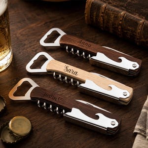 May include: Three multi-functional wine openers with wooden handles and stainless steel components. Each tool features a bottle opener, a corkscrew, and a small blade. The handles are engraved with the names Anna, Sara, and Justin with a heart icon.
