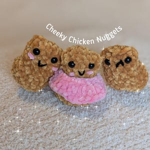 May include: Three handmade, plush chicken nuggets with embroidered faces. One nugget wears a pink ruffle. The text "Cheeky Chicken Nuggets" is arched above the nuggets. The bottom right corner has the text "@cozycomfyloops".
