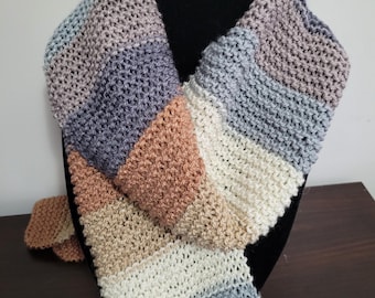 May include: A handmade, striped scarf in shades of blue, tan, white, and mauve. The scarf is displayed on a black mannequin head. The scarf is made of a soft, textured yarn, and the design is a simple, yet elegant, pattern.