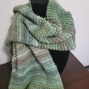 May include: A green and brown knitted scarf with a gradient pattern. The scarf is draped over a black mannequin.