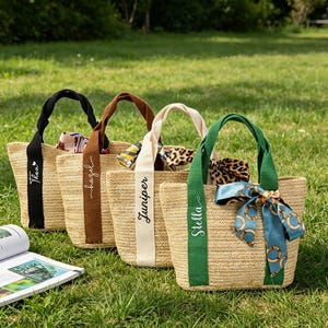 May include: Four woven straw tote bags with different colored handles and personalized name tags. Each bag has a decorative scarf tied to the handle. The names on the tags are Thea, hazel, Juniper, and Stella.