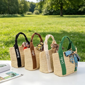 May include: Four woven straw tote bags with different colored handles and personalized names: Rowan, Willow, Hazel, and Stella. Each bag has a decorative scarf tied to the handle. The bags are sitting on a white surface with a green grassy background.