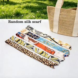 May include: Assortment of silk scarves with various patterns, including animal print and geometric designs. The scarves are in shades of brown, orange, blue, and cream. A woven tote bag with cream-colored handles is in the background. Text on the image reads "Random silk scarf."