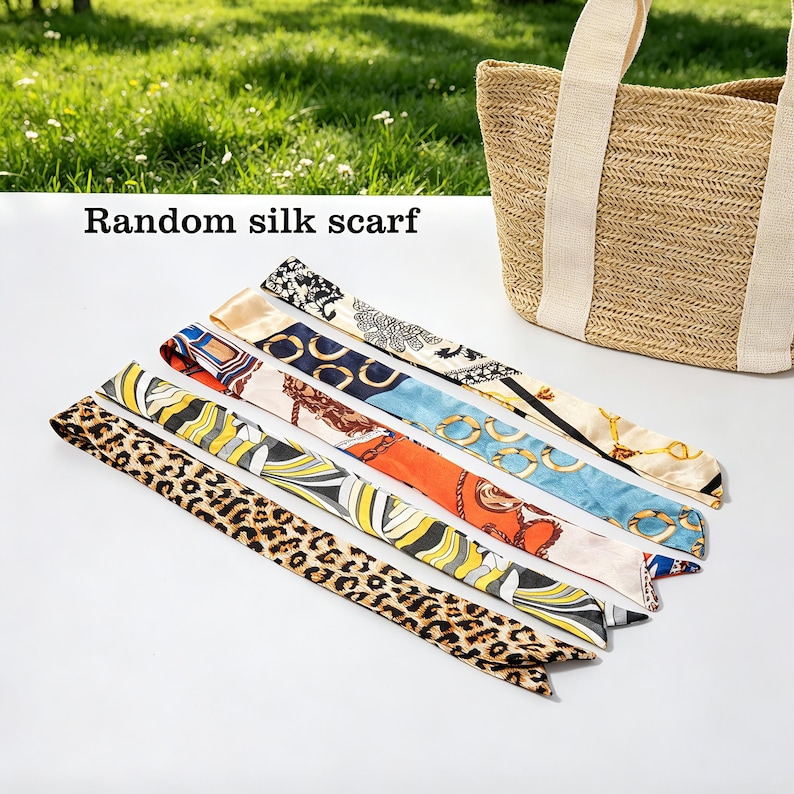 May include: Assortment of silk scarves with various patterns, including animal print and geometric designs. The scarves are in shades of brown, orange, blue, and cream. A woven tote bag with cream-colored handles is in the background. Text on the image reads "Random silk scarf."