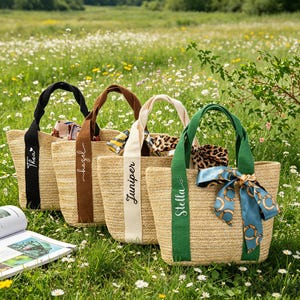 May include: Four woven straw tote bags with different colored handles and ribbons. Each bag has a name printed on the ribbon: Thea, hazel, Juniper, and Stella. The bags are decorated with scarves and bows.