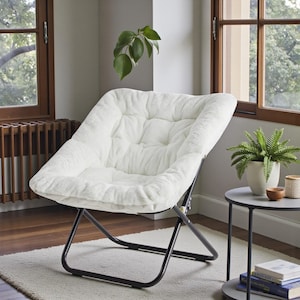 May include: A white, plush, folding chair with a black metal frame. The chair has a tufted seat and backrest. The chair is positioned in front of a window, with a small side table and potted plant nearby.