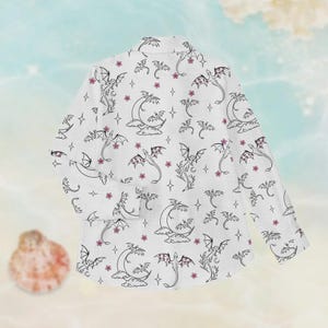 May include: White blazer with a repeating pattern of black dragons, moons, stars, and pink flowers. The blazer has long sleeves and a classic collar. The design is whimsical and fantasy-themed.