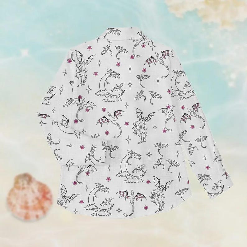 May include: White blazer with a repeating pattern of black dragons, moons, stars, and pink flowers. The blazer has long sleeves and a classic collar. The design is whimsical and fantasy-themed.