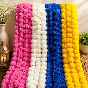 May include: Four artificial flower garlands in pink, white, blue, and yellow, featuring dense, spherical blossoms. The text ARTIFICIAL FLOWER GARLAND, HANDMADE, VIBRANT, REUSABLE, PERFECT FOR DECORATION, VIBRANT COLORS, LIGHTWEIGHT & DURABLE, REUSABLE & ECO-FRIENDLY is visible.