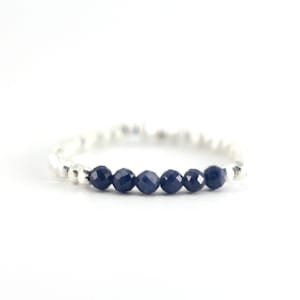 May include: A silver ring with a row of dark blue gemstone beads.