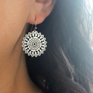 May include: Silver earrings with a delicate, circular design featuring a mandala pattern.