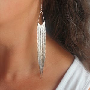 May include: Silver dangle earrings with a geometric design and a chain fringe.