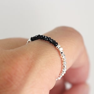 May include: A silver and black beaded ring worn on a finger.