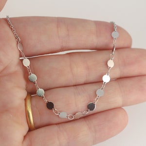 May include: A silver chain necklace with small round silver discs. The necklace is delicate and simple.