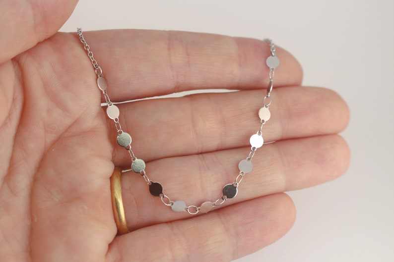May include: A silver chain necklace with small round silver discs. The necklace is delicate and simple.