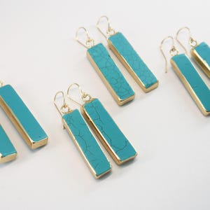 May include: Set of six turquoise and gold dangle earrings. Each earring features a rectangular turquoise stone with gold accents.