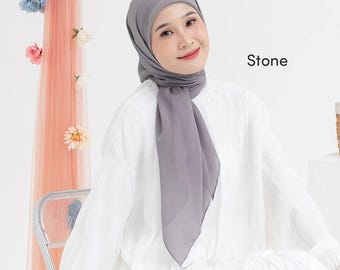 May include: A woman wearing a gray hijab and a white blouse. The hijab is draped around the head and shoulders, with the word "Stone" in white text on the right side of the image. The background includes a sheer peach-colored fabric and decorative flowers.