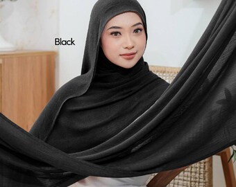 May include: A black hijab, draped elegantly, with the word "Black" in the upper left corner. The fabric appears soft and flowing, with subtle texture. The hijab is worn by a person seated in a chair.