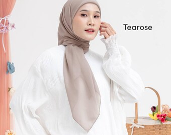 May include: A woman wearing a light brown hijab and a white blouse. The hijab is draped over the head and shoulders. The word "Tearose" is printed on the right side of the image.