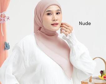 May include: A woman wearing a nude-colored hijab and a white blouse. The hijab is draped over the head and shoulders, with the word "Nude" in black text to the right. The blouse has long sleeves with ruffled cuffs.