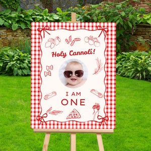 Può includere: Un cartello con un bordo a scacchi rosso e bianco e un centro color crema. Il cartello presenta un bambino con occhiali da sole, le parole "Holy Cannoli!" e "I AM ONE", insieme a illustrazioni di pasta e cibo italiano.