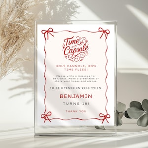 May include: A clear acrylic frame holds a white card with red text and accents. The card reads "Time Capsule" with the text "Holy Cannoli, How Time Flies!" and "Benjamin Turns 18!" The frame is on a white surface.