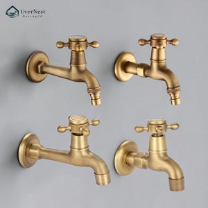Op de afbeelding: Vier antieke messing waterkranen met kruisvormige handgrepen zijn op een grijze muur gemonteerd. De kranen hebben een vintage esthetiek, met een warme, verouderde afwerking. Het EverNest DesingCo-logo staat linksboven.