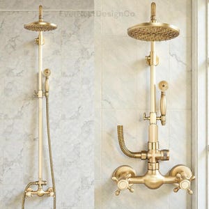 Puede incluir: Un conjunto de ducha de estilo vintage en latón dorado. Incluye un rociador redondo, una ducha de mano, una manguera flexible y grifos de cruz. El conjunto está instalado en una pared de azulejos blancos. El texto "EverestDesignCo" es visible.