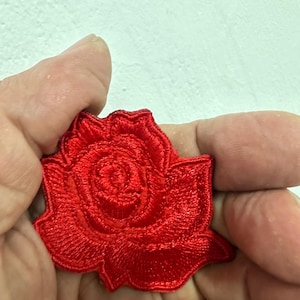 Può includere: Una toppa a forma di rosa ricamata di colore rosso vivo. La toppa presenta cuciture dettagliate, che mostrano i petali e la forma generale del fiore. La rosa è un design floreale classico, adatto a vari progetti artigianali o abbellimenti di abbigliamento.