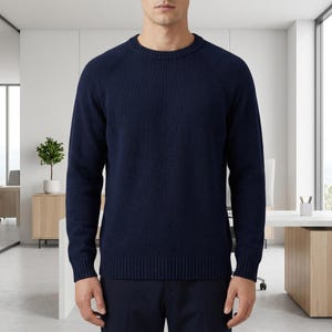 May include: Navy blue crew neck jumper. The jumper features long sleeves and ribbed detailing at the hem and cuffs. The model is wearing the jumper in an office setting.