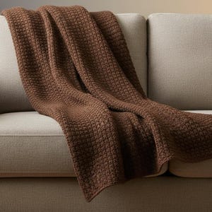 May include: A brown textured throw blanket draped over a beige sofa. The blanket has a woven pattern and is made of a soft material. The sofa has a modern design with a neutral color scheme.