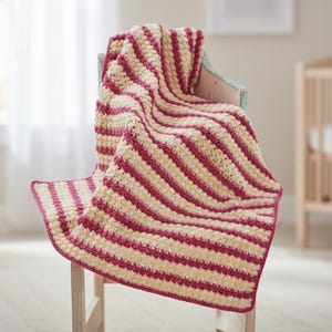 May include: A handmade, striped crochet blanket in cream and burgundy, draped over a light blue chair. The blanket features thick, horizontal stripes and a matching burgundy border. The cozy, soft blanket is suitable for a nursery or home decor.