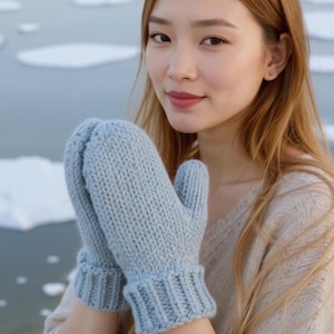 May include: A pair of pale blue knitted mittens. The mittens are made from a soft, textured yarn with a ribbed cuff. These mittens are designed for warmth in cold weather. The mittens are a light blue colour.