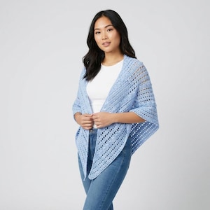 May include: A light blue crochet shawl with an open weave design. The shawl is worn over a white top and blue jeans. The shawl has a triangular shape and drapes over the shoulders.