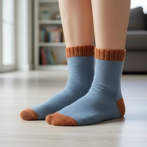 May include: A pair of blue socks with brown cuffs, heels, and toes. The socks are ribbed and appear to be made of a soft, warm material. The socks are worn by a person indoors.