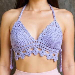 Könnte beinhalten: Lavendelfarbenes Häkeltop mit Halter-Träger und floralem Design am unteren Rand. Das Top hat eine dreieckige Brust und Bindebänder am Hals und am Rücken. Das handgefertigte Top ist ein stilvolles Kleidungsstück.